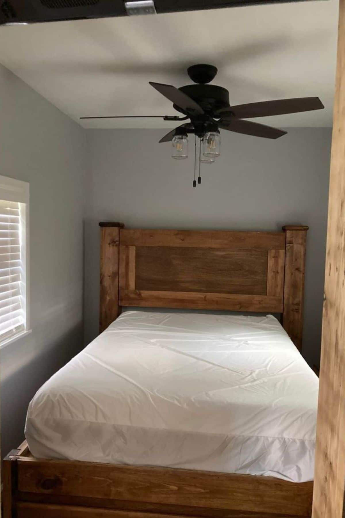 Wooden headboard on bed in room with gray walls and ceiling fan
