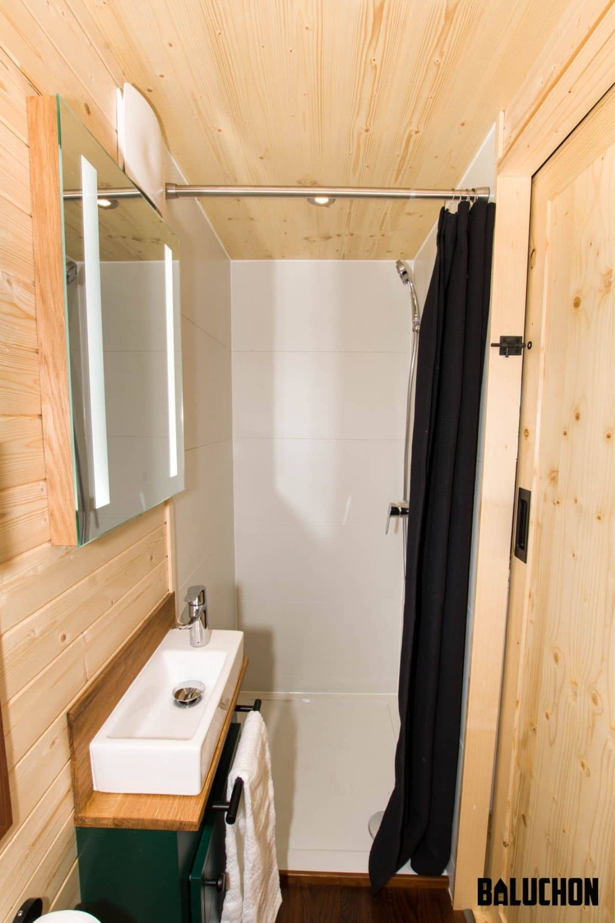 Shower stall in light wood bathroom with black curtain
