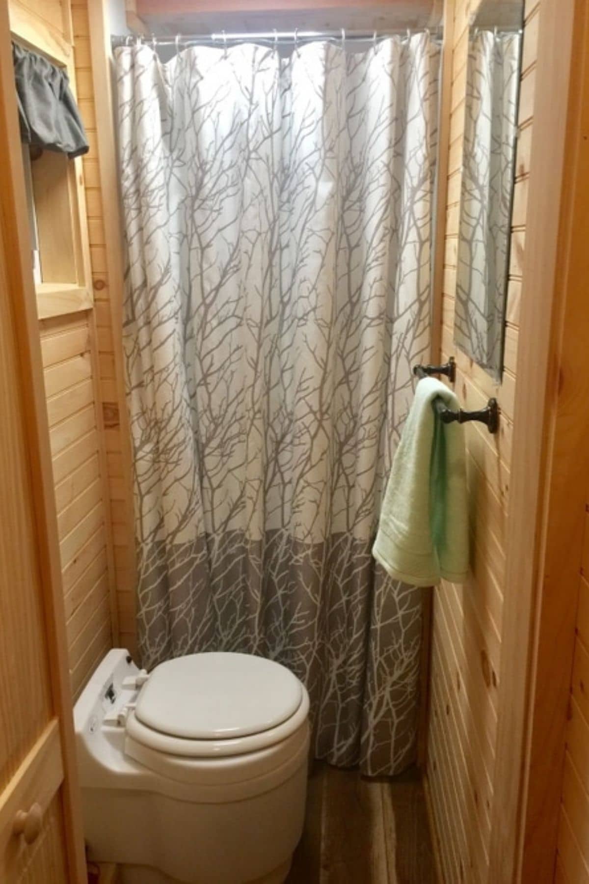 compost toilet in front of shower with green towel on rack beside it