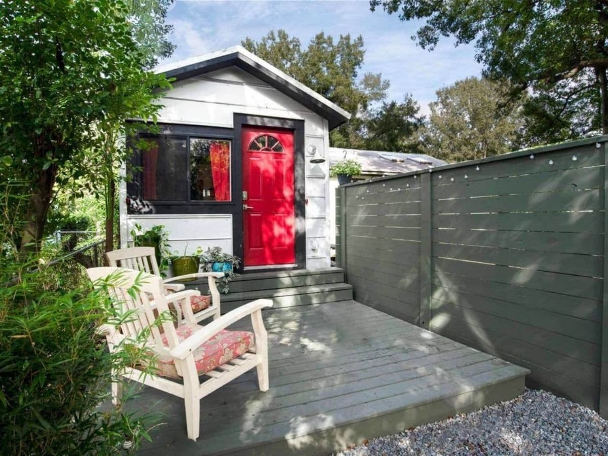 white tiny house with red door against gray fence