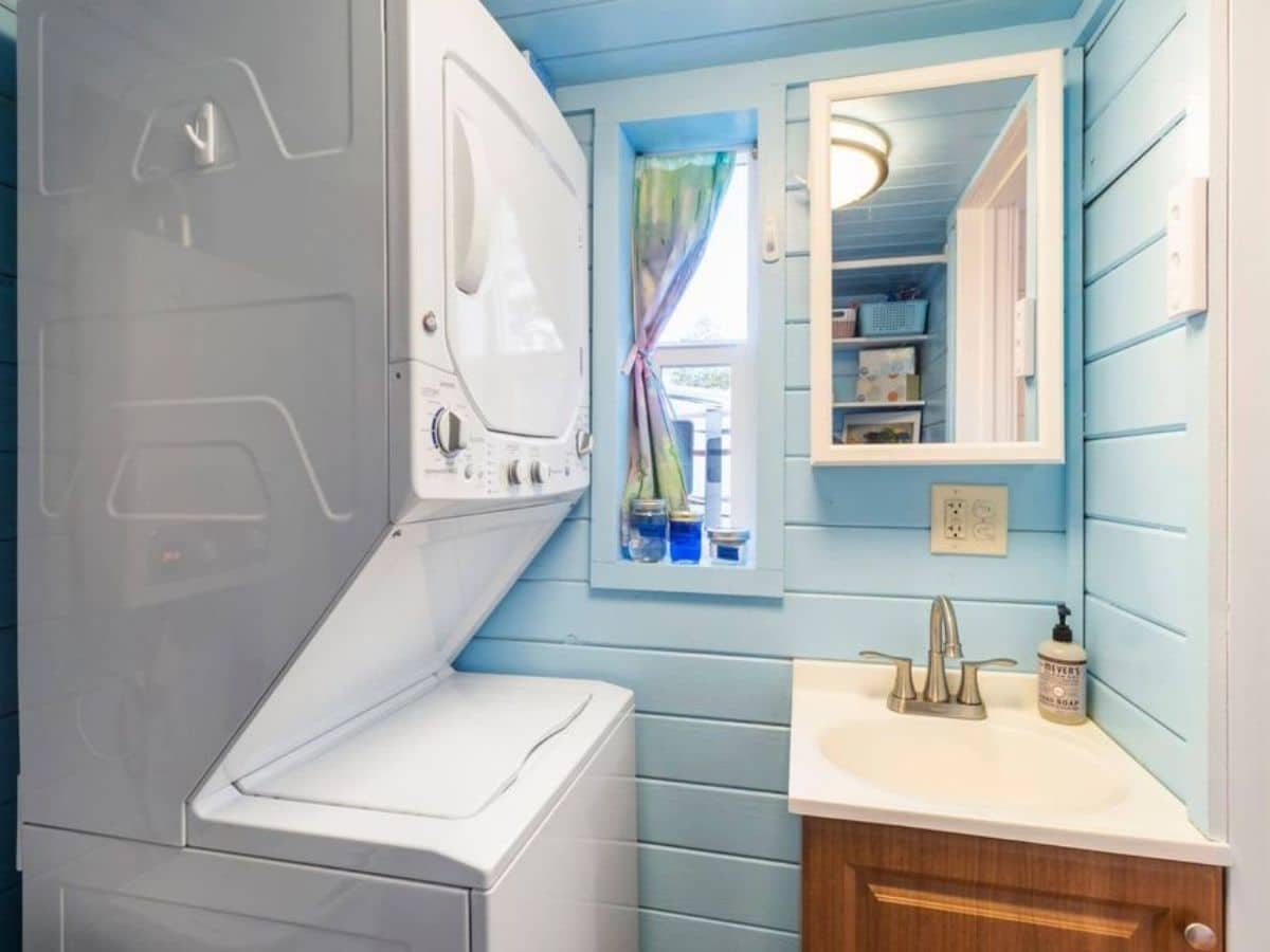 stacking white washer and dryer next to white sink and blue walls in bathroom