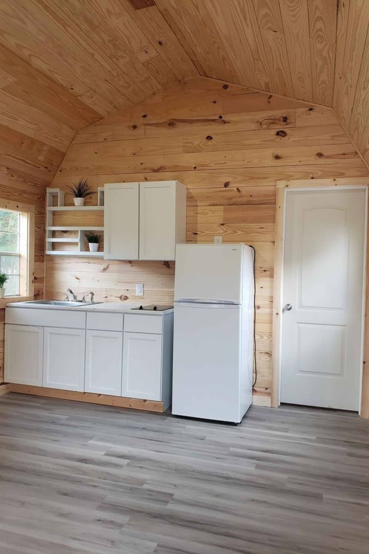 white cabinets and refrigerator against wood wall next to white door