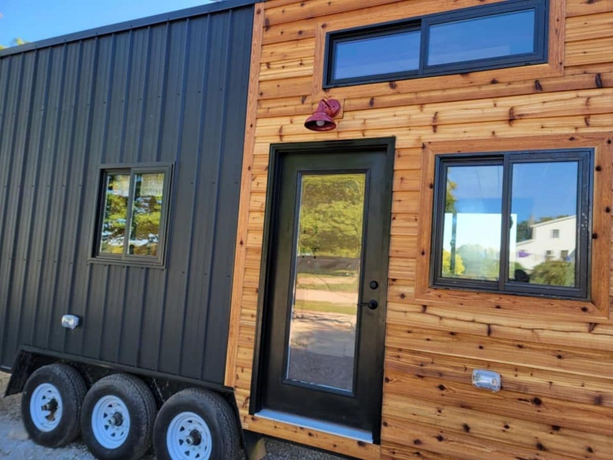 side of tiny home showing black siding and black door in wood siding insert