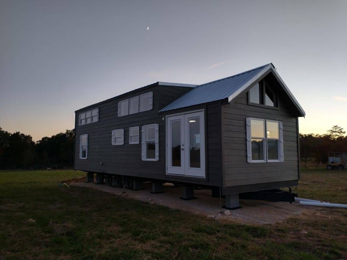 tiny home with dark siding and white trim on concrete slab in field