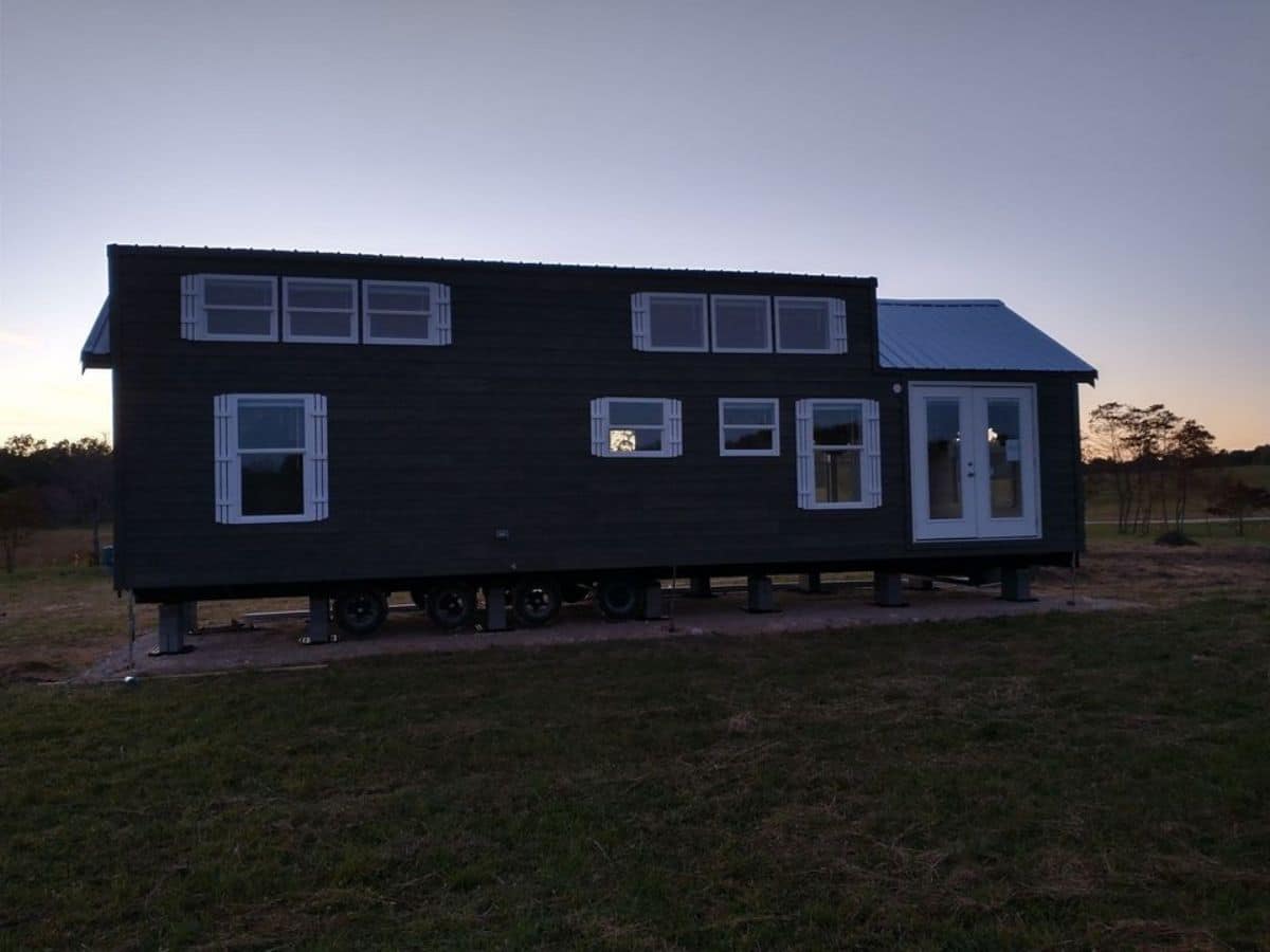 side of dark tiny home on wheels with long windows on top half of home
