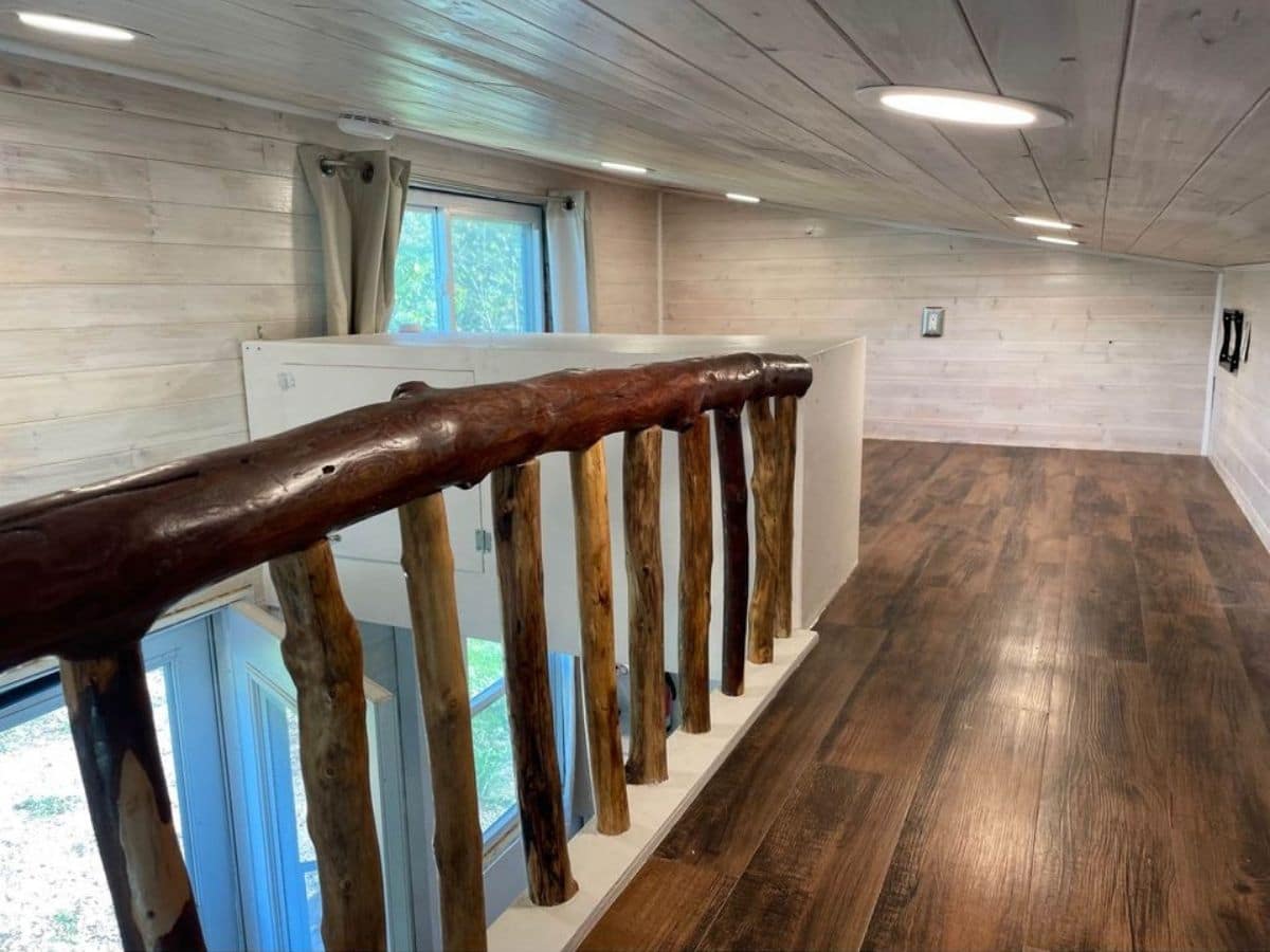 stained wood limb railing on left with wood floor on bottom of loft