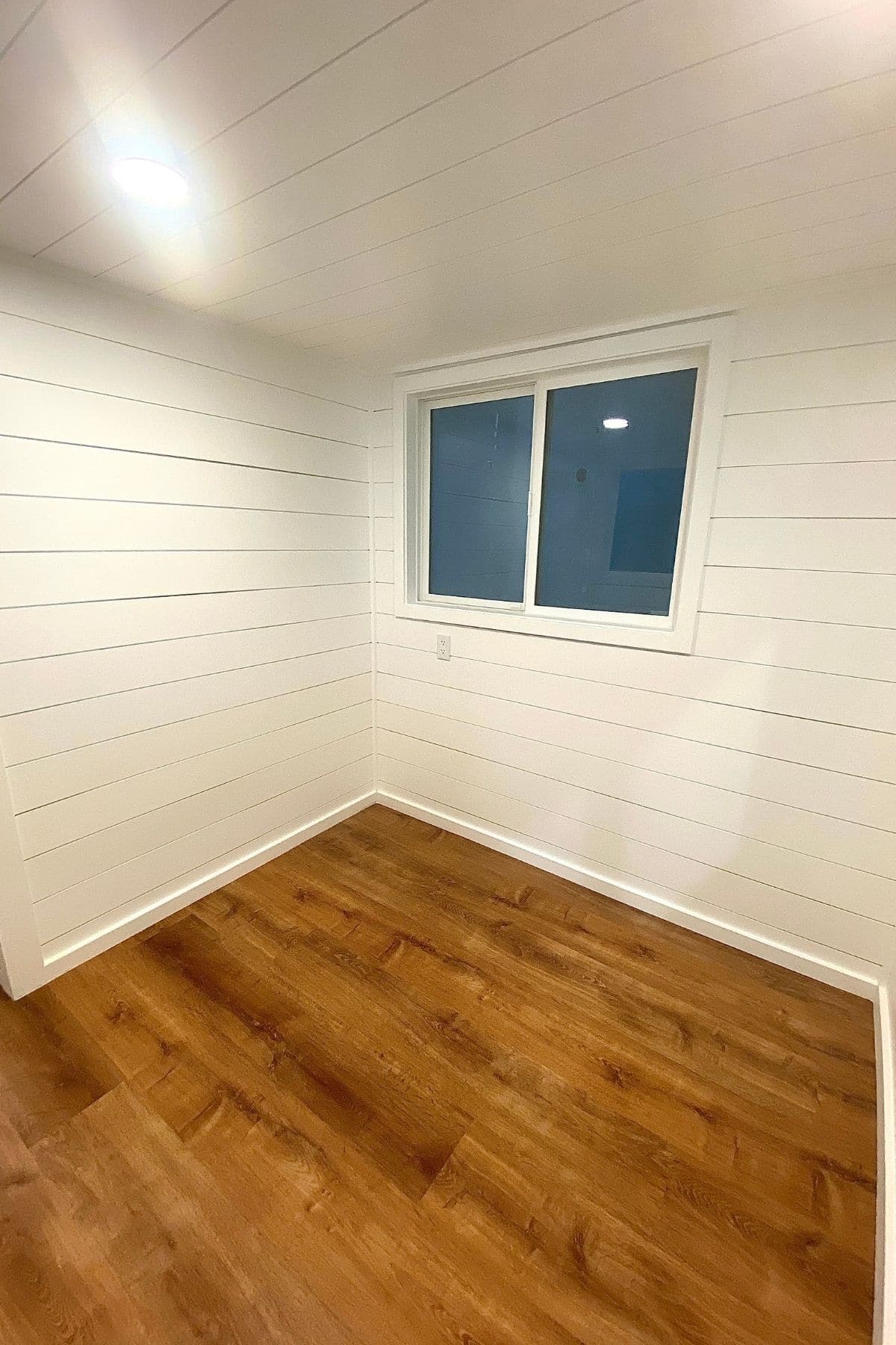 living room with white shiplap walls a single window and wood floors