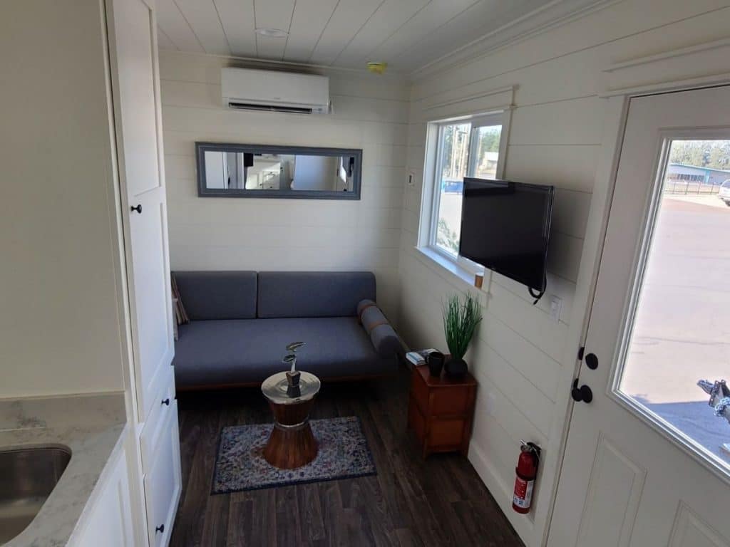 view toward end of tiny home with blue sofa against wall and tv mounted on right wall