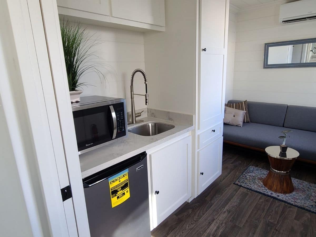 kitchenette to the left with white cabinets mini fridge and sink