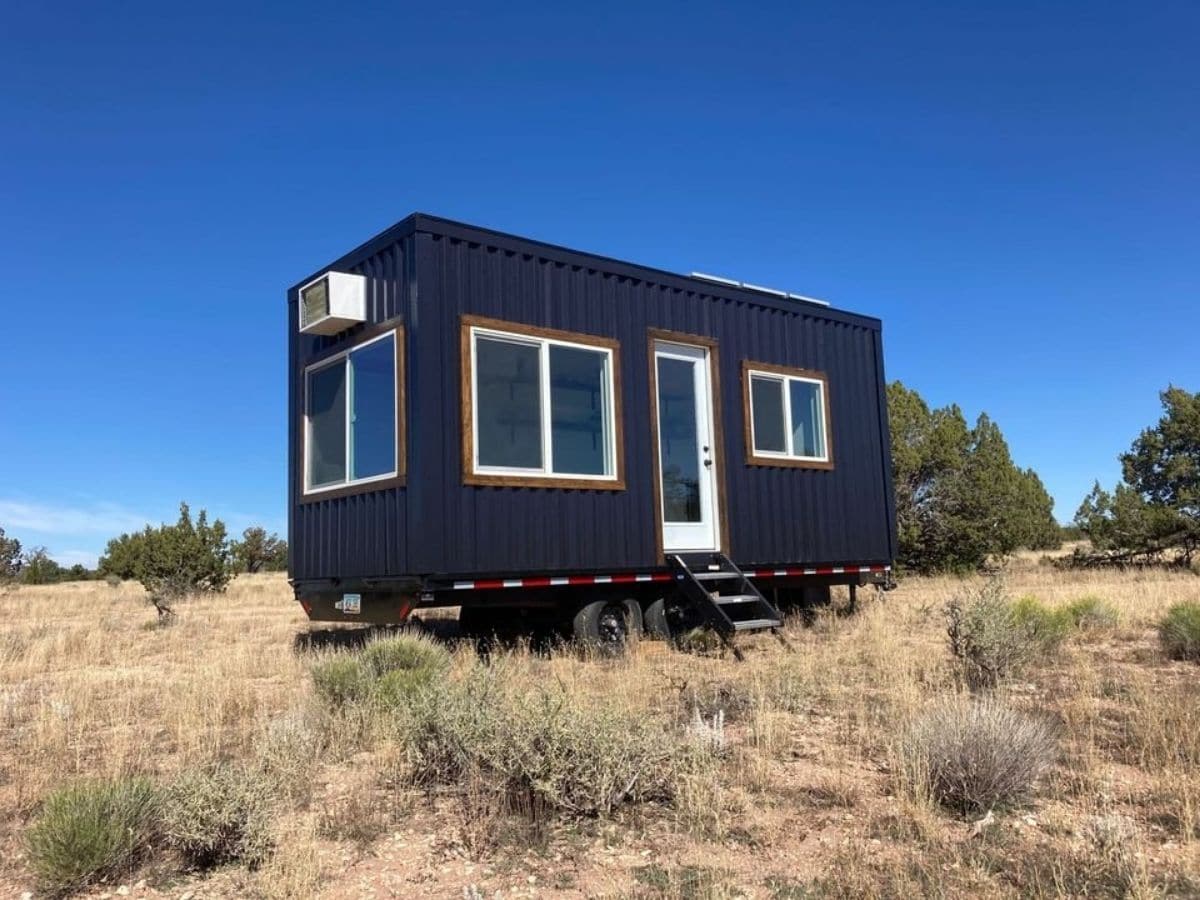 blue tiny home with white trim sitting in field of grass