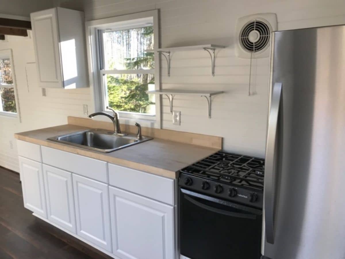 stainless steel refrigerator and black stove in foreground next to white cabinets
