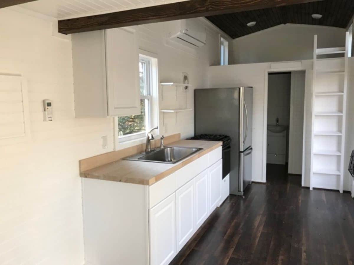 kitchen in tiny home to left with white cabinets and butcher block countertop