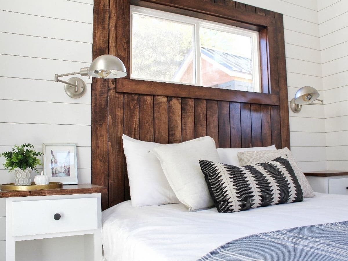wood headboard and window above bed with lamp on wall
