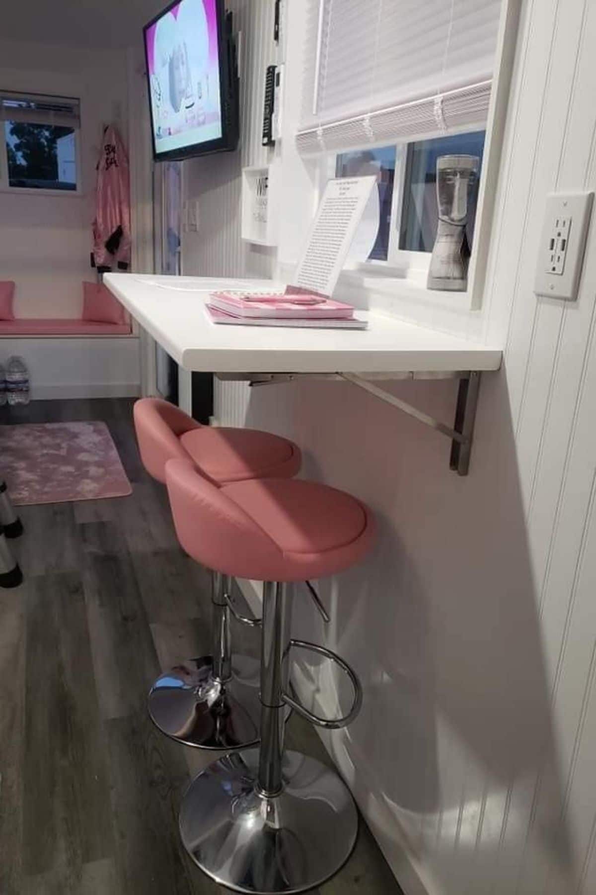 pink bucket stools underneath white counter attached to wall under window in tiny living room