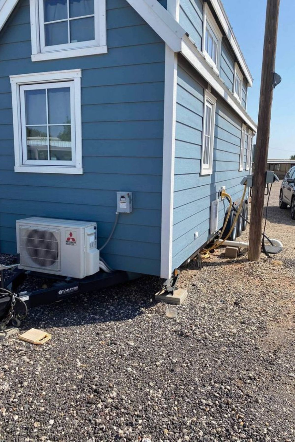 back of blue tiny home with light trim and AC on back end