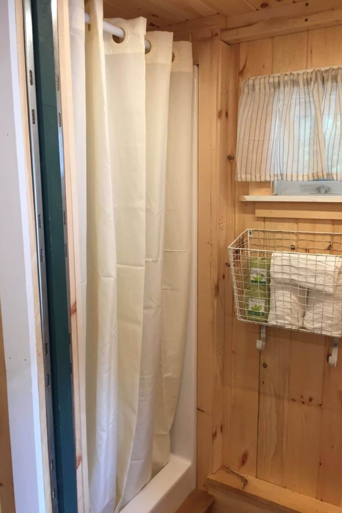 shower stall with white curtain on left and basket hanging beneath window on middle right