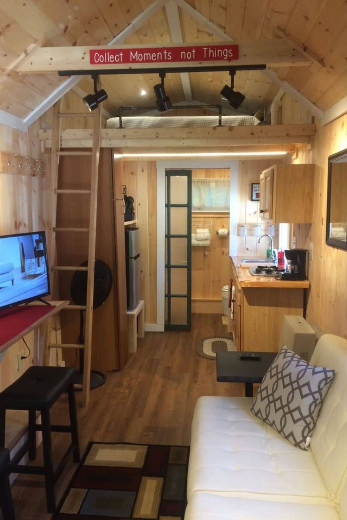 entry to tiny home with white sofa on right and loft above kitchen