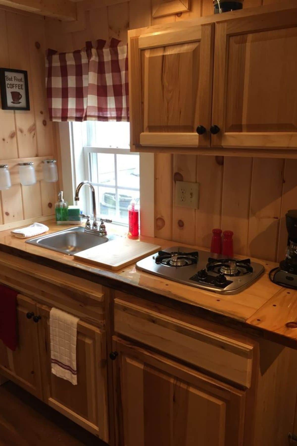wood cabinets in kitchen with checked curtain on window above sink