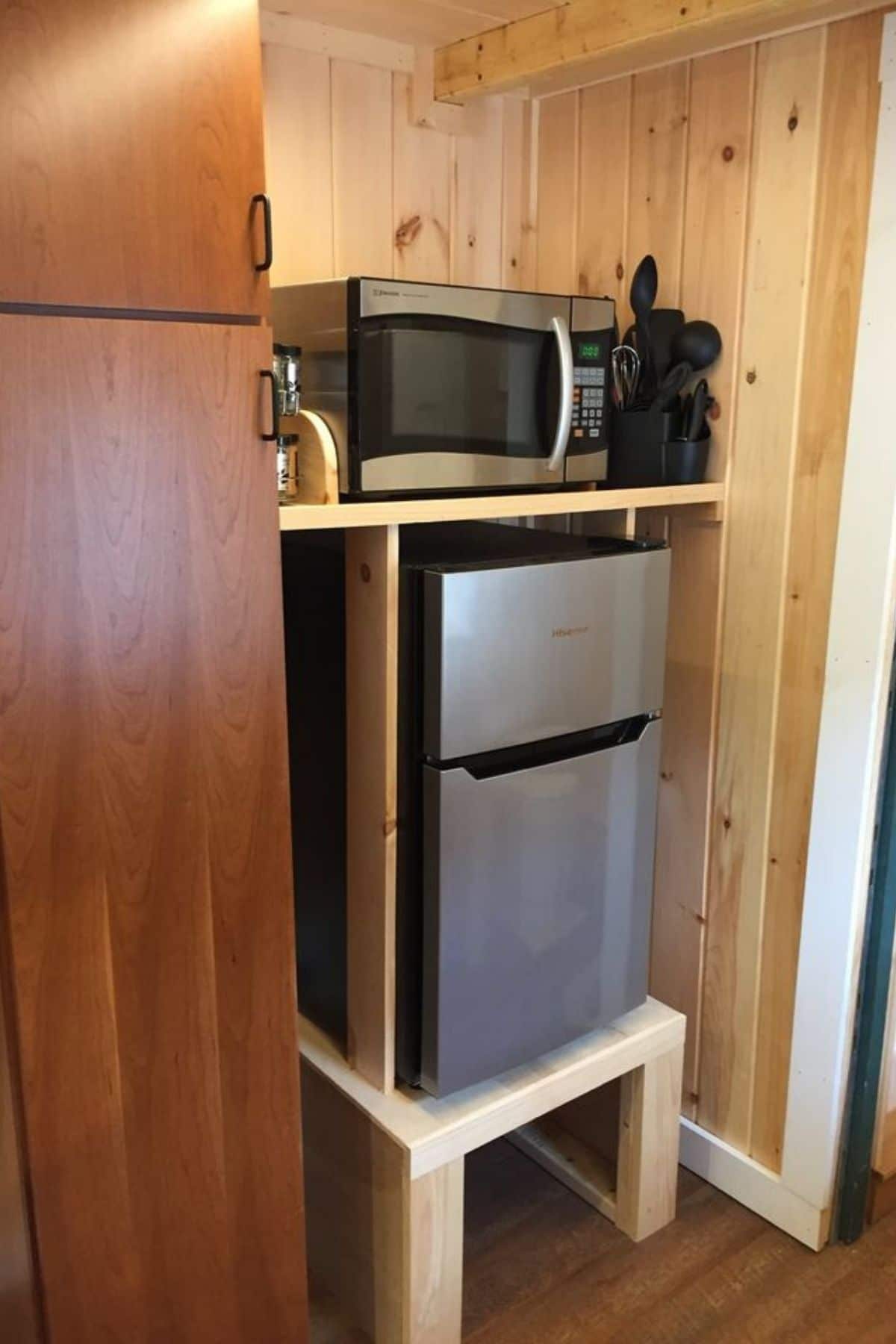 mini refrigerator on shelf below microwave by pantry