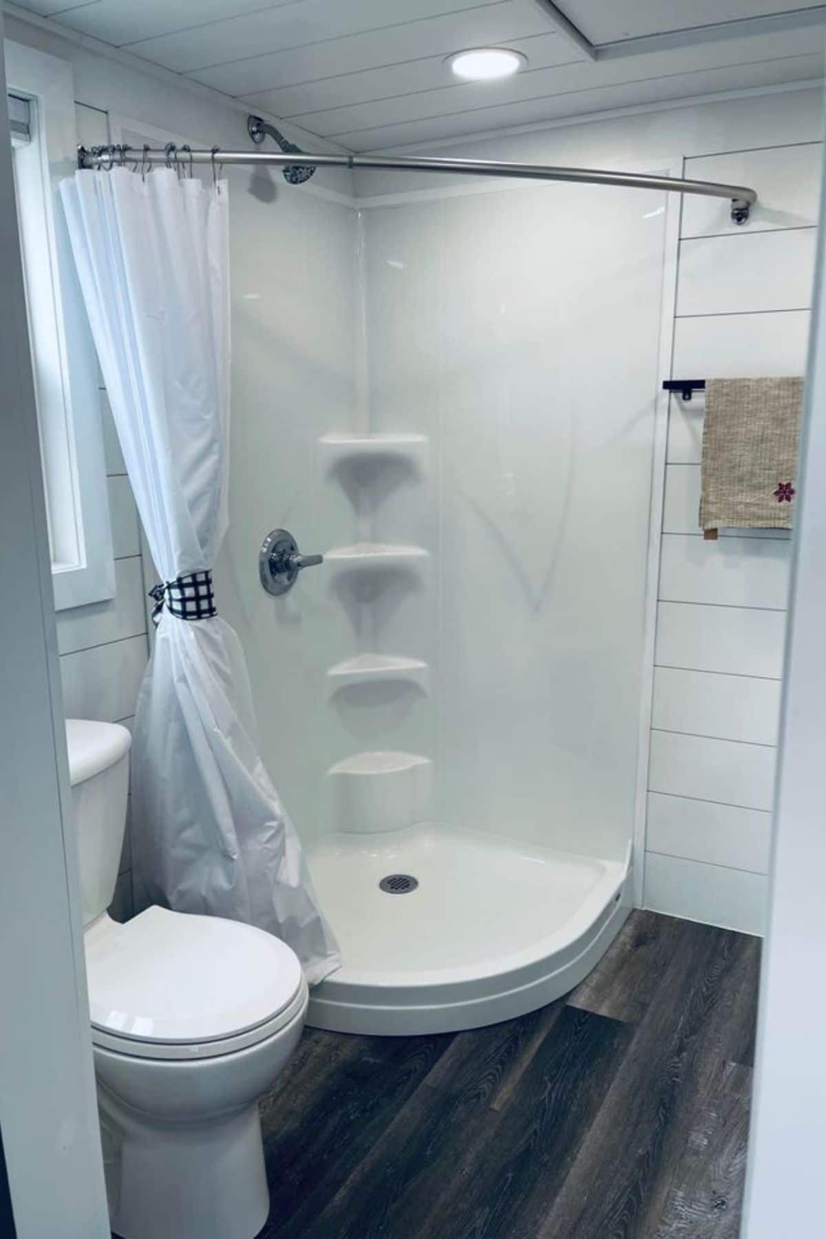 corner white shower with shelves against wall next to white flush toilet