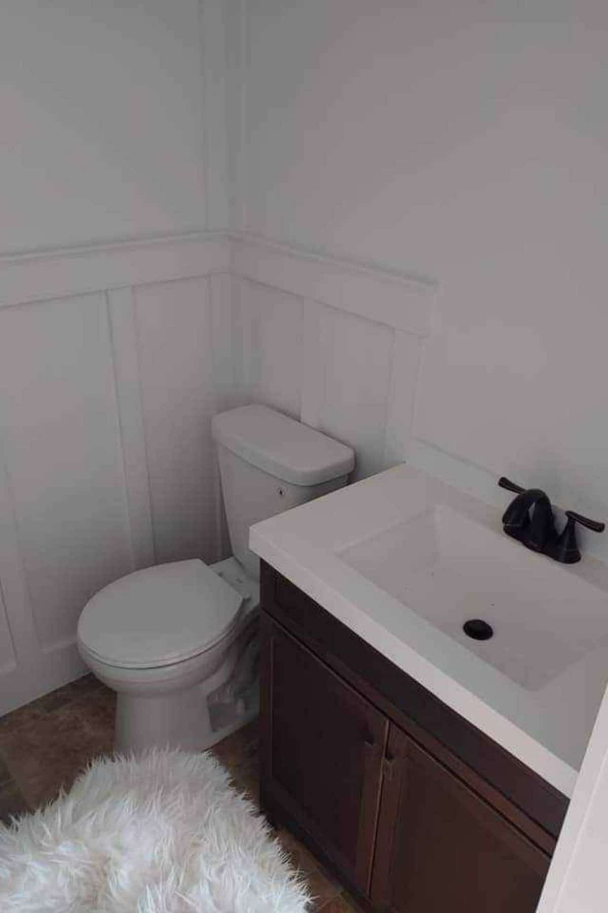 flush toilet next to brown cabinet with white sink and countertop
