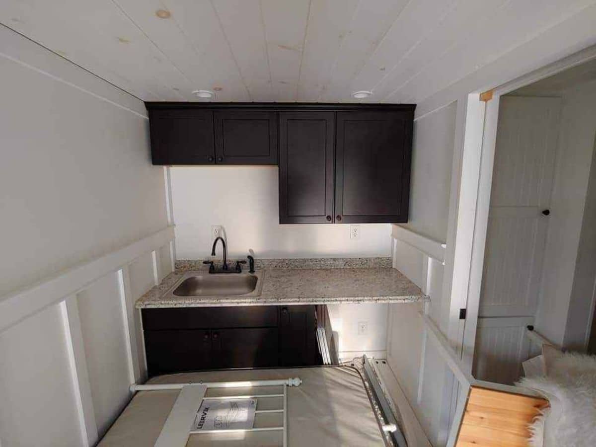 bed in floor near kitchen with black cabinets against far wall