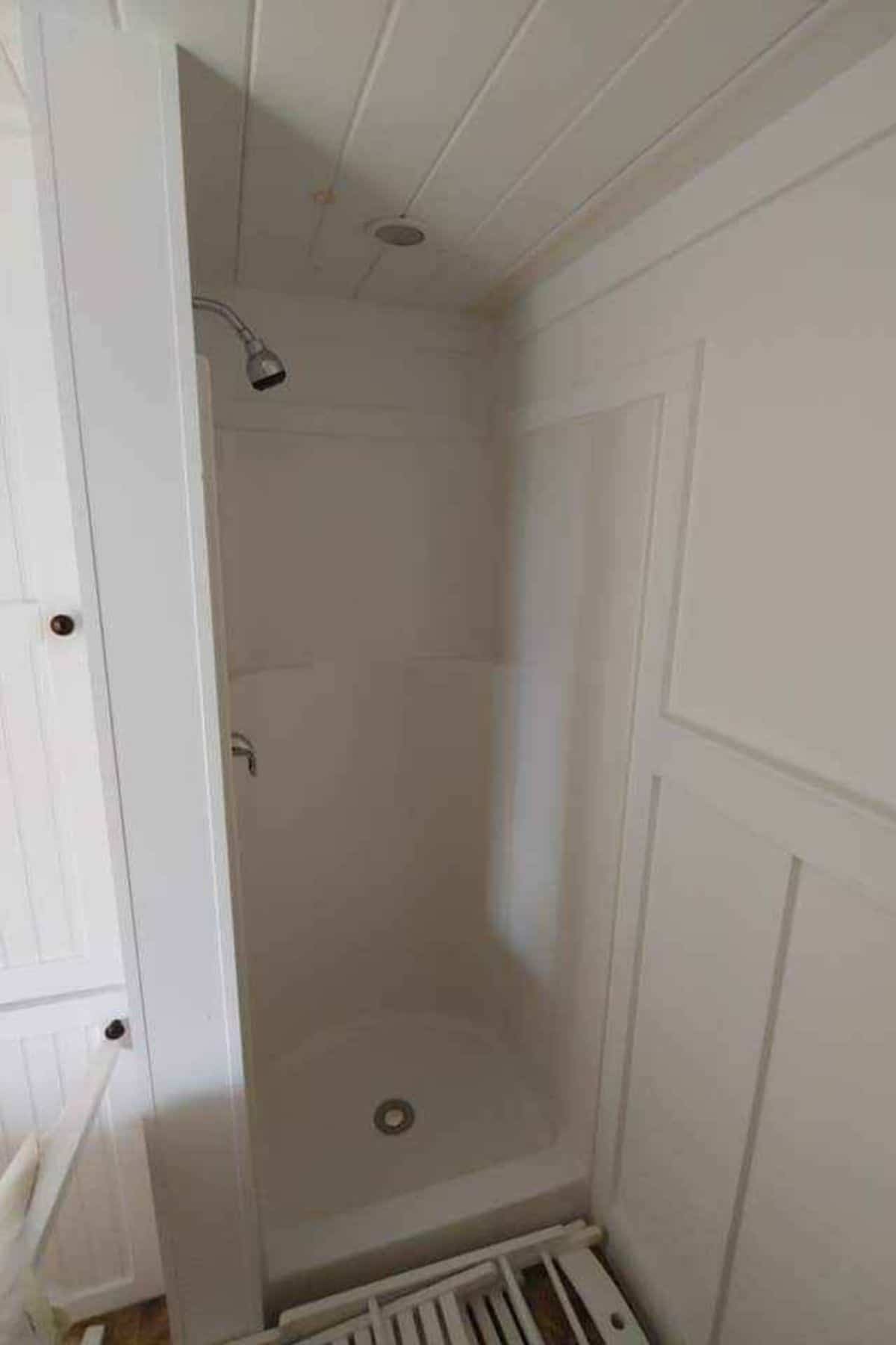 white shower stall in corner of bathroom with white walls