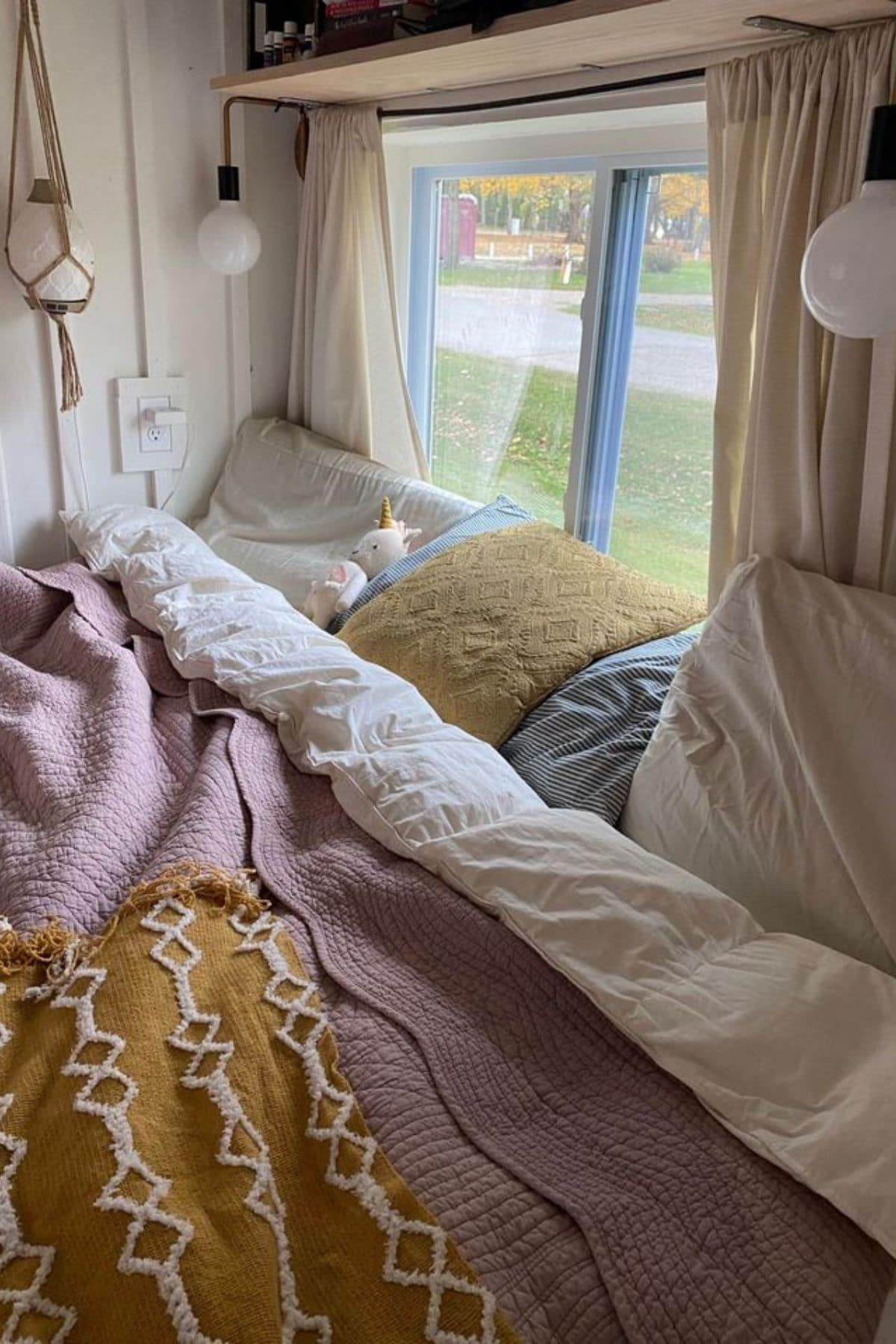 bed with pink and yellow blankets underneath window