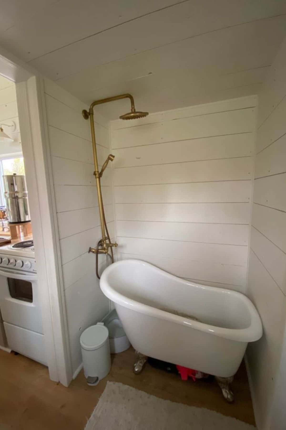 small white clawfoot bathtub beneath gold shower head against white shiplap wall