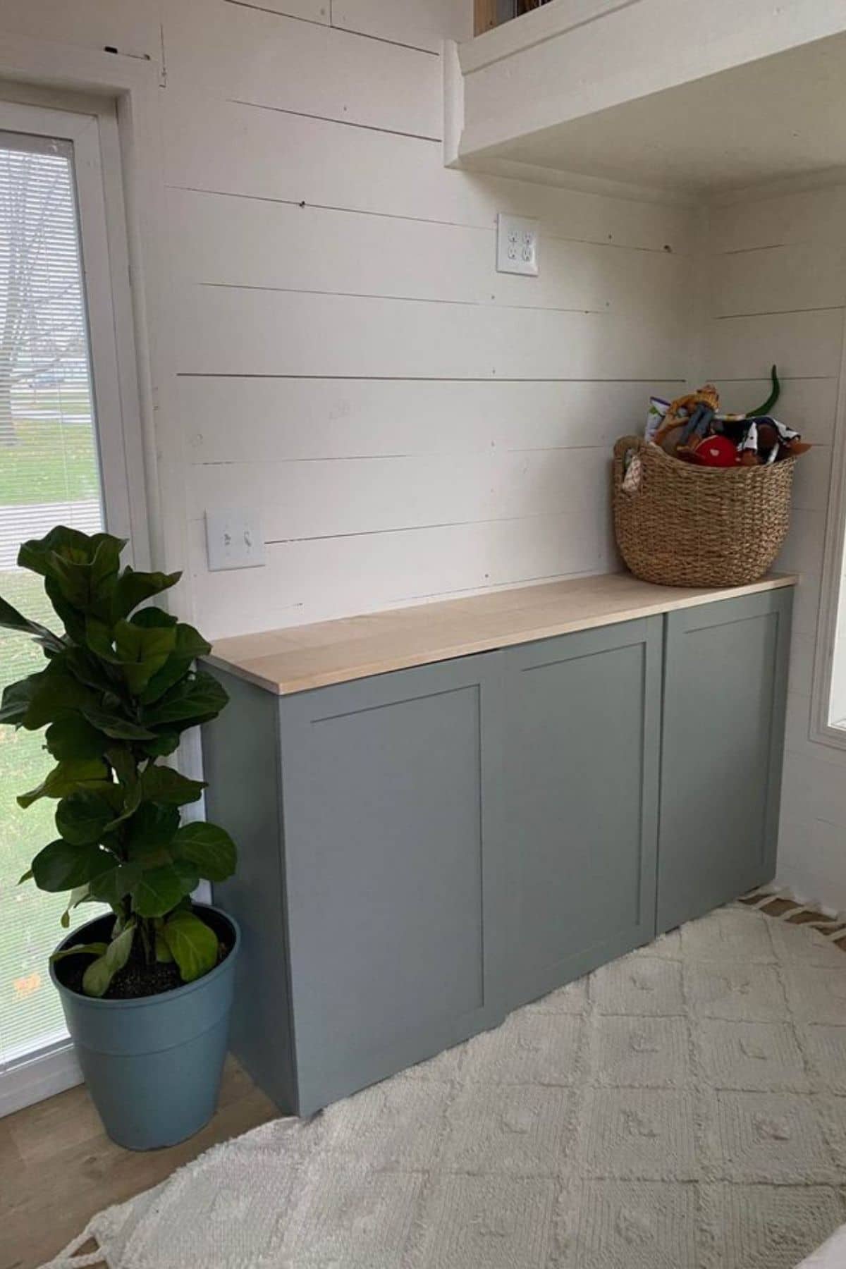 gray and wood cabinet against white shiplap wall with potted plant on side