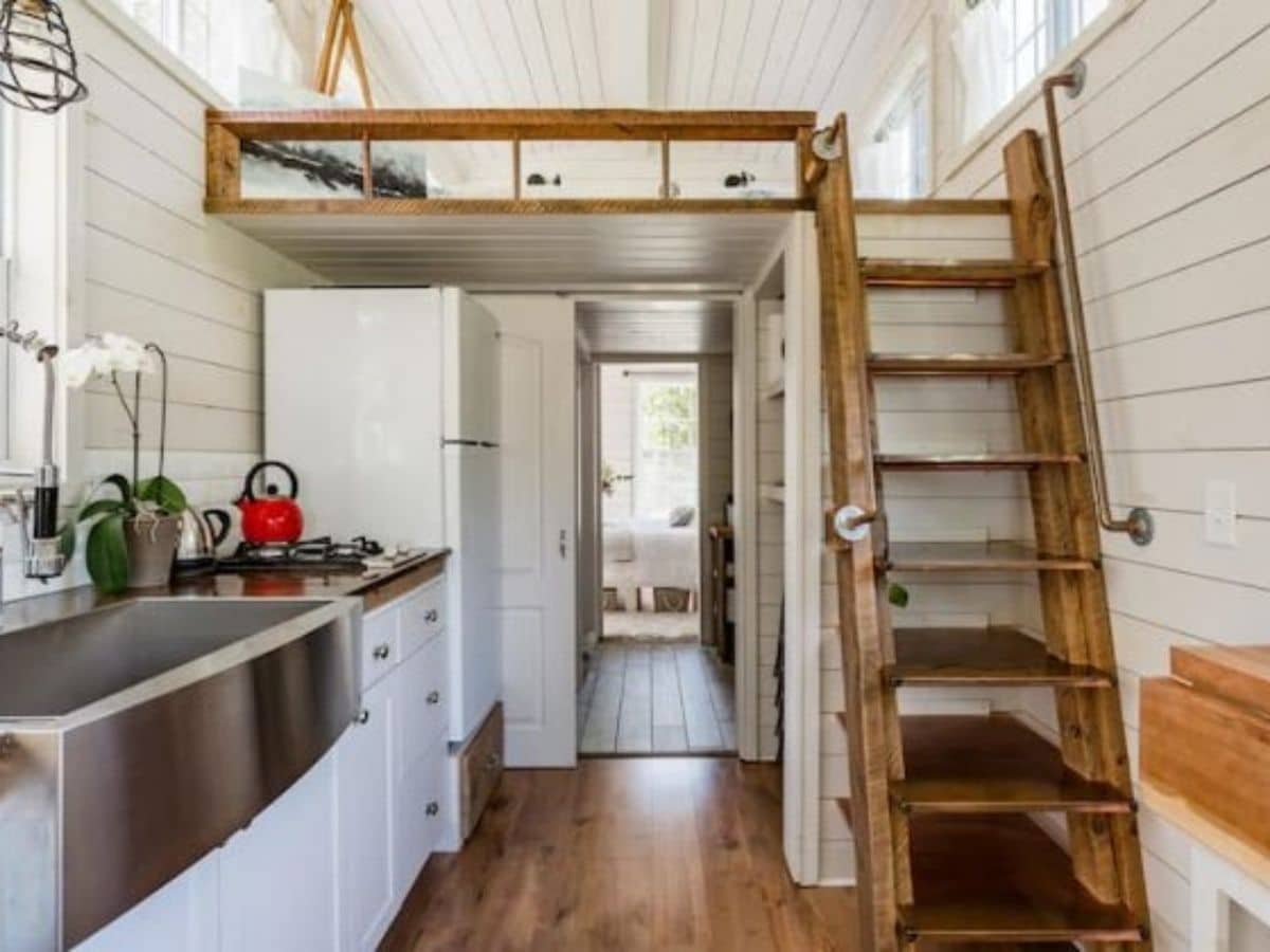 wooden stairs on right with kitchenette on left and loft above with white shiplap all around