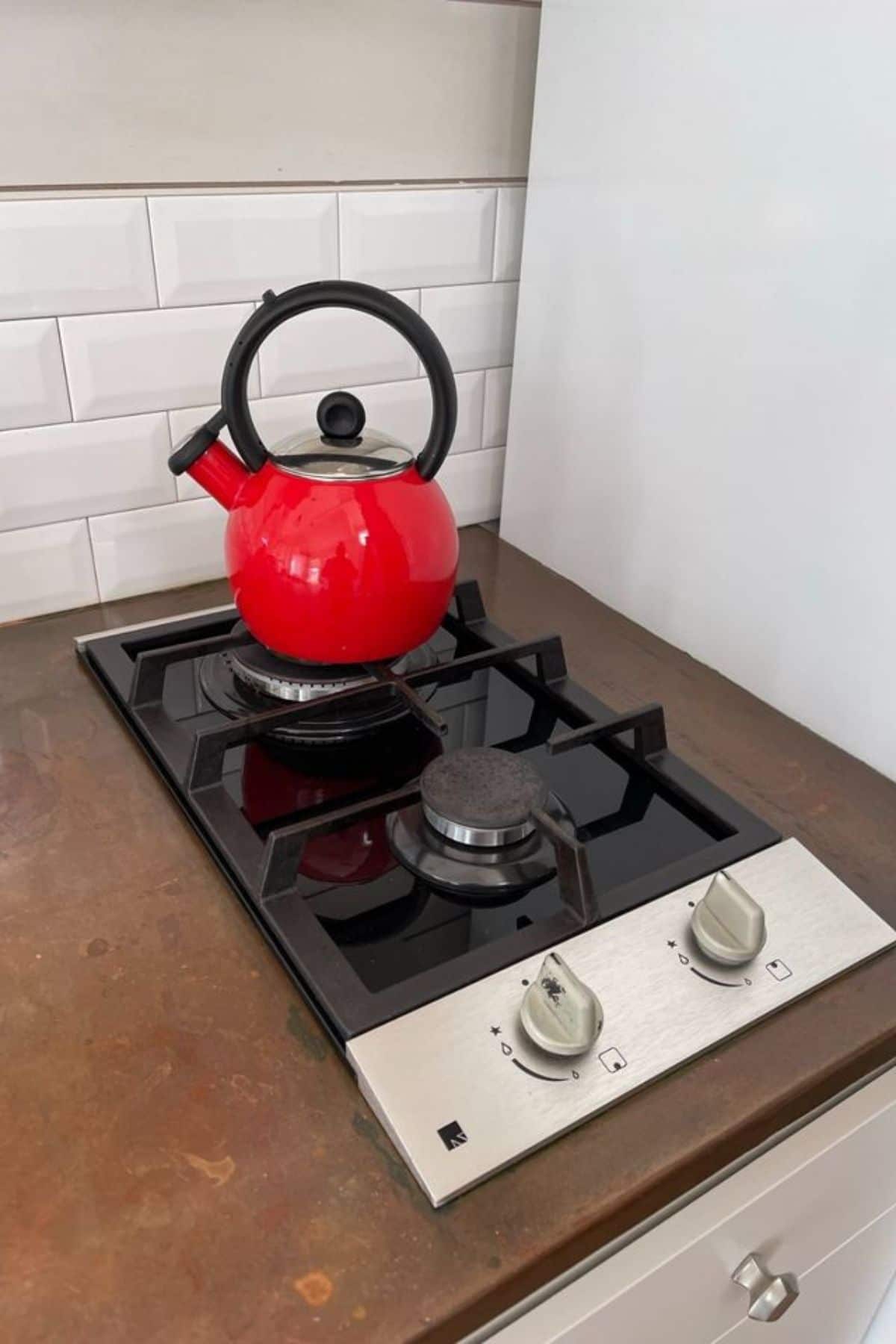 two burner gas cooktop with stainless steel knobs and red kettle on the back