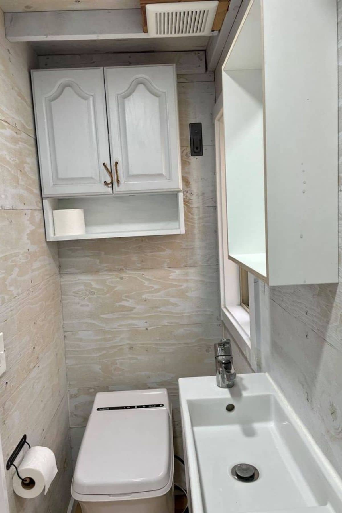 white cabinet on wall above incinerator toilet next to white sink in bathroom