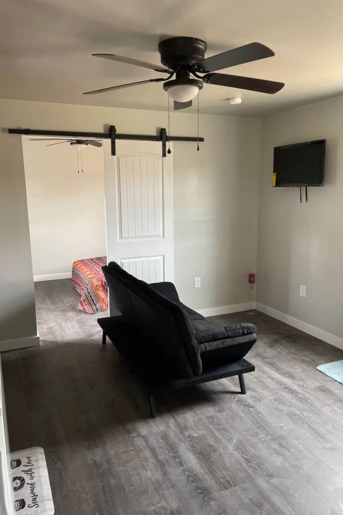 black sofa in middle of room below ceiling fan with tv on wall