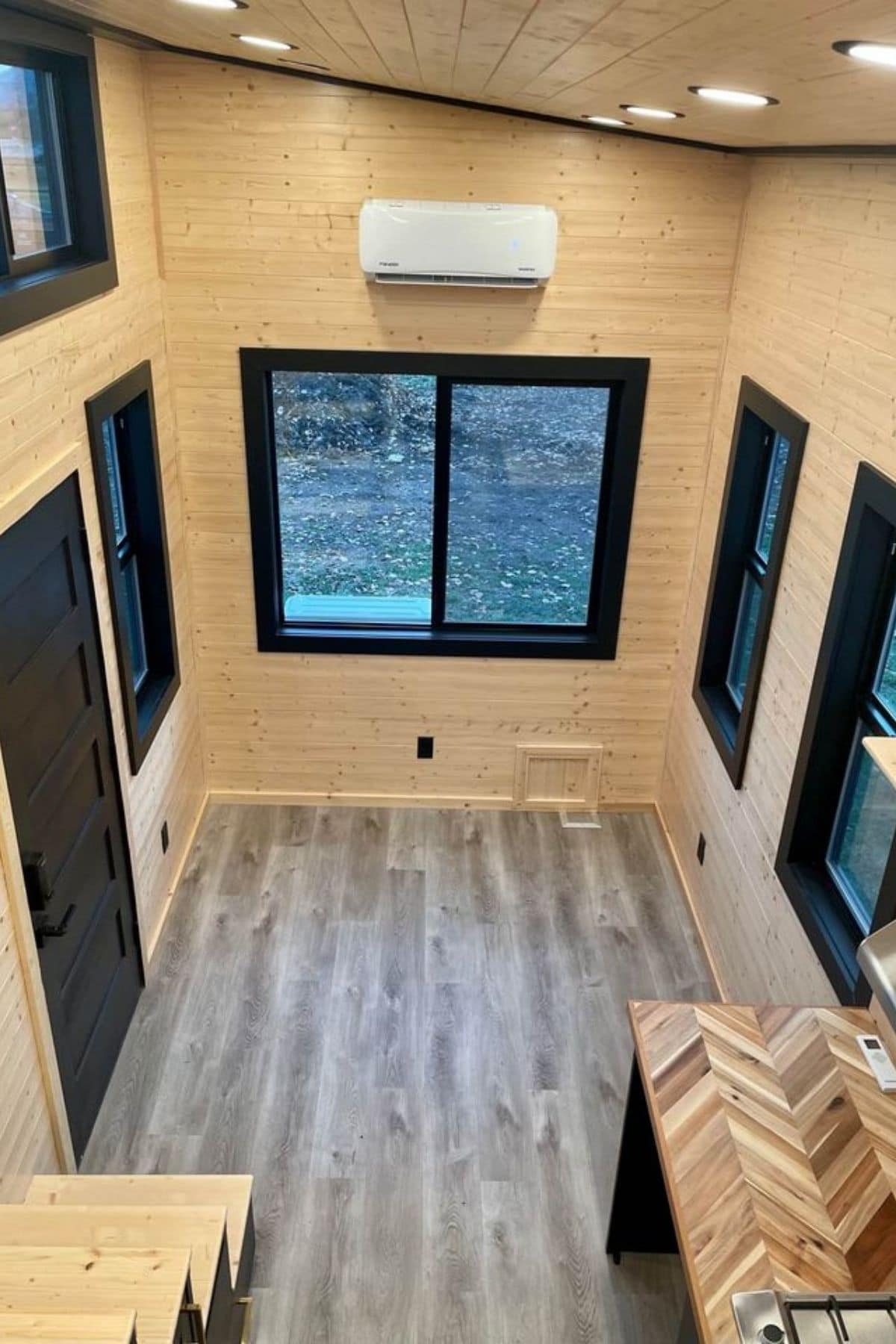 view from loft down into main living space with light wood walls, black trim, and gray wood flooring