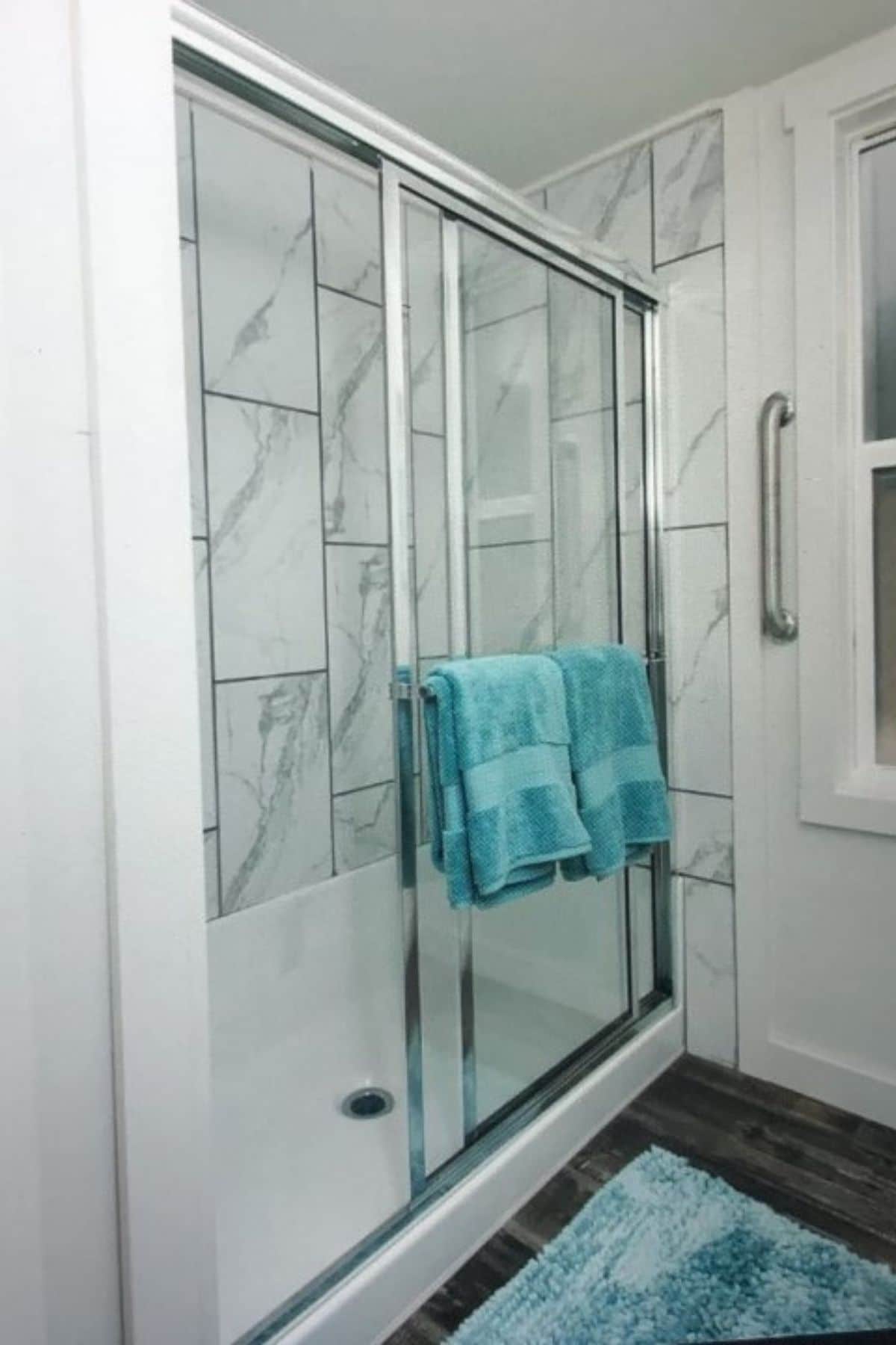 marble tiled shower with glass door an teal towels on door