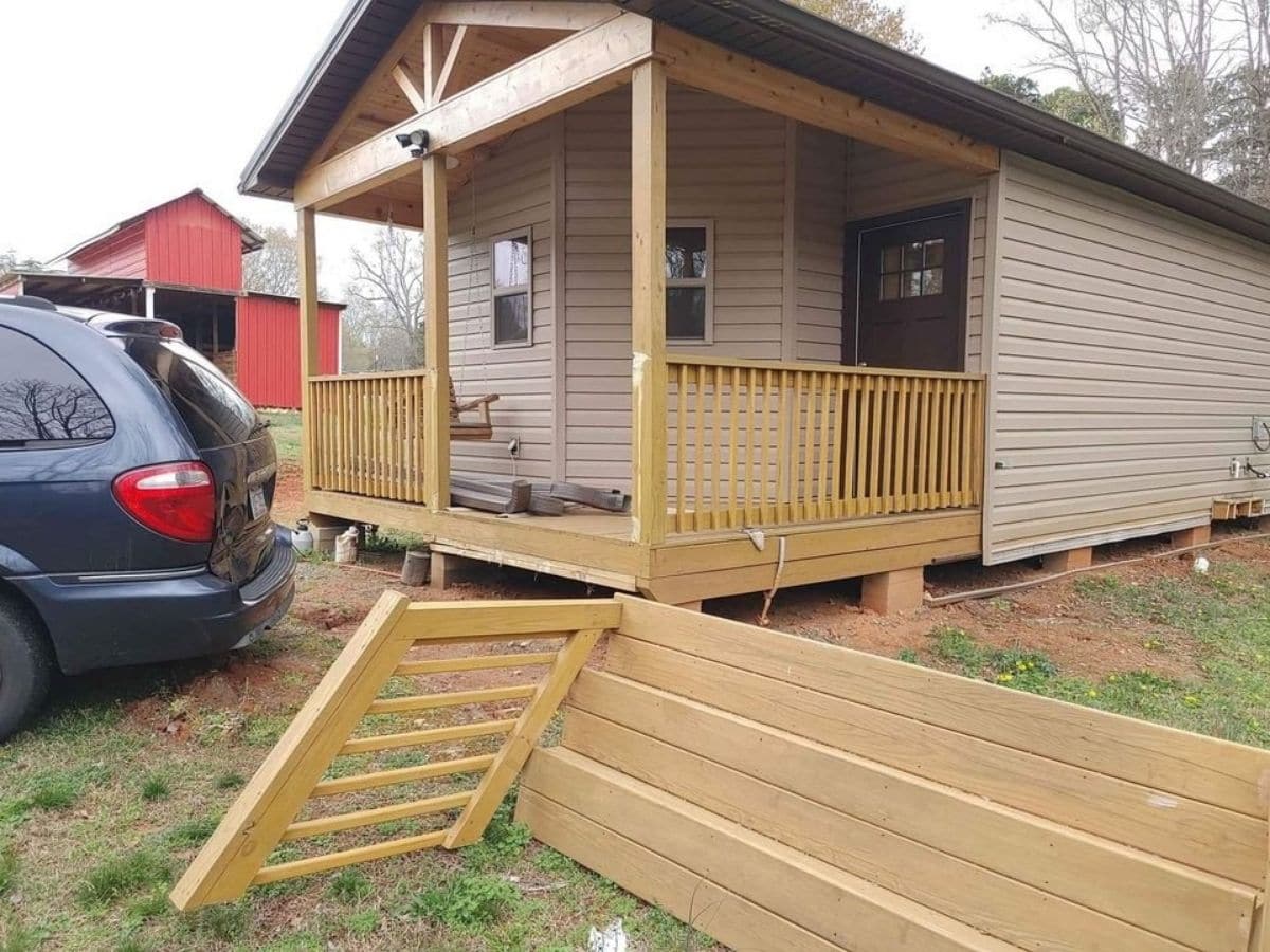 front porch of tan tiny home with porch parts on ground in front