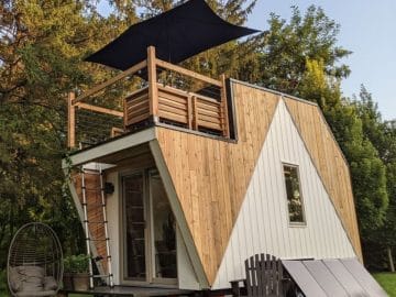 tiny house with two light colors of siding and deck on top