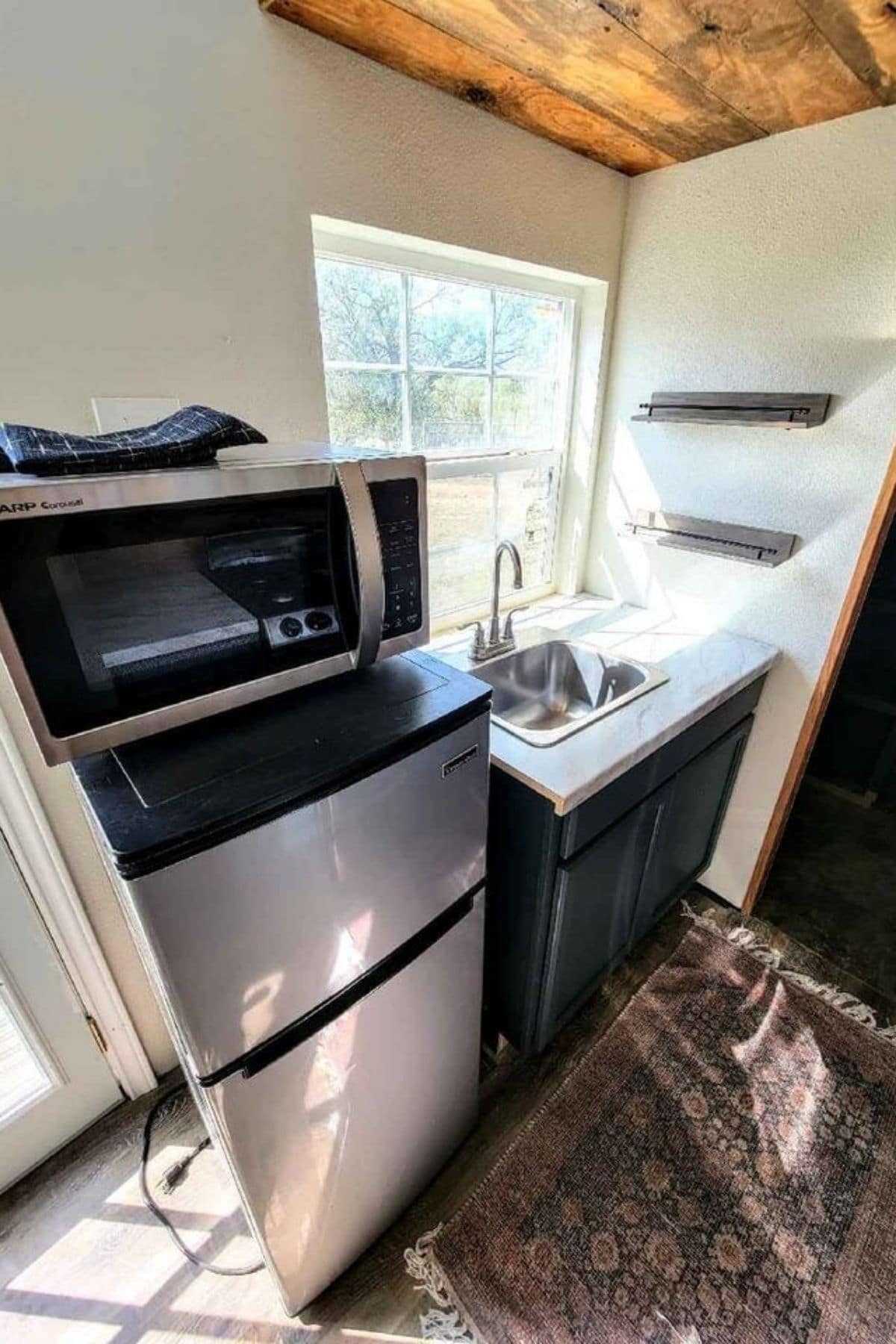 Stainless steel refrigerator with microwave on top next to blue cabinets with white counters and sink