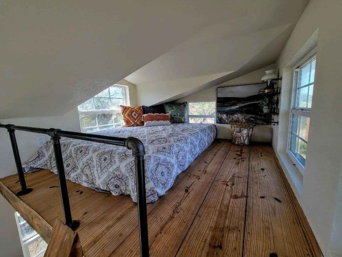 twin mattress in loft by fake dormer window with black railing in foreground