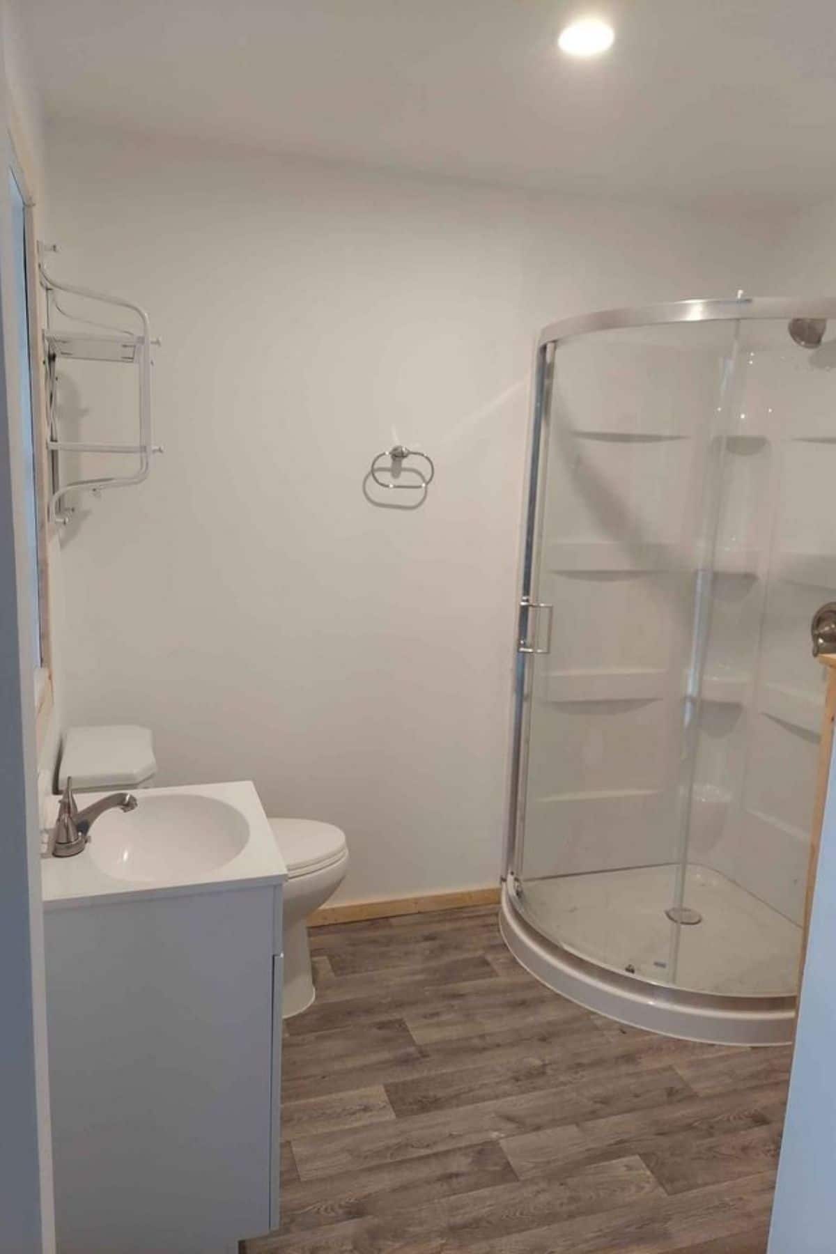 round glass shower stall in corner of white walled bathroom