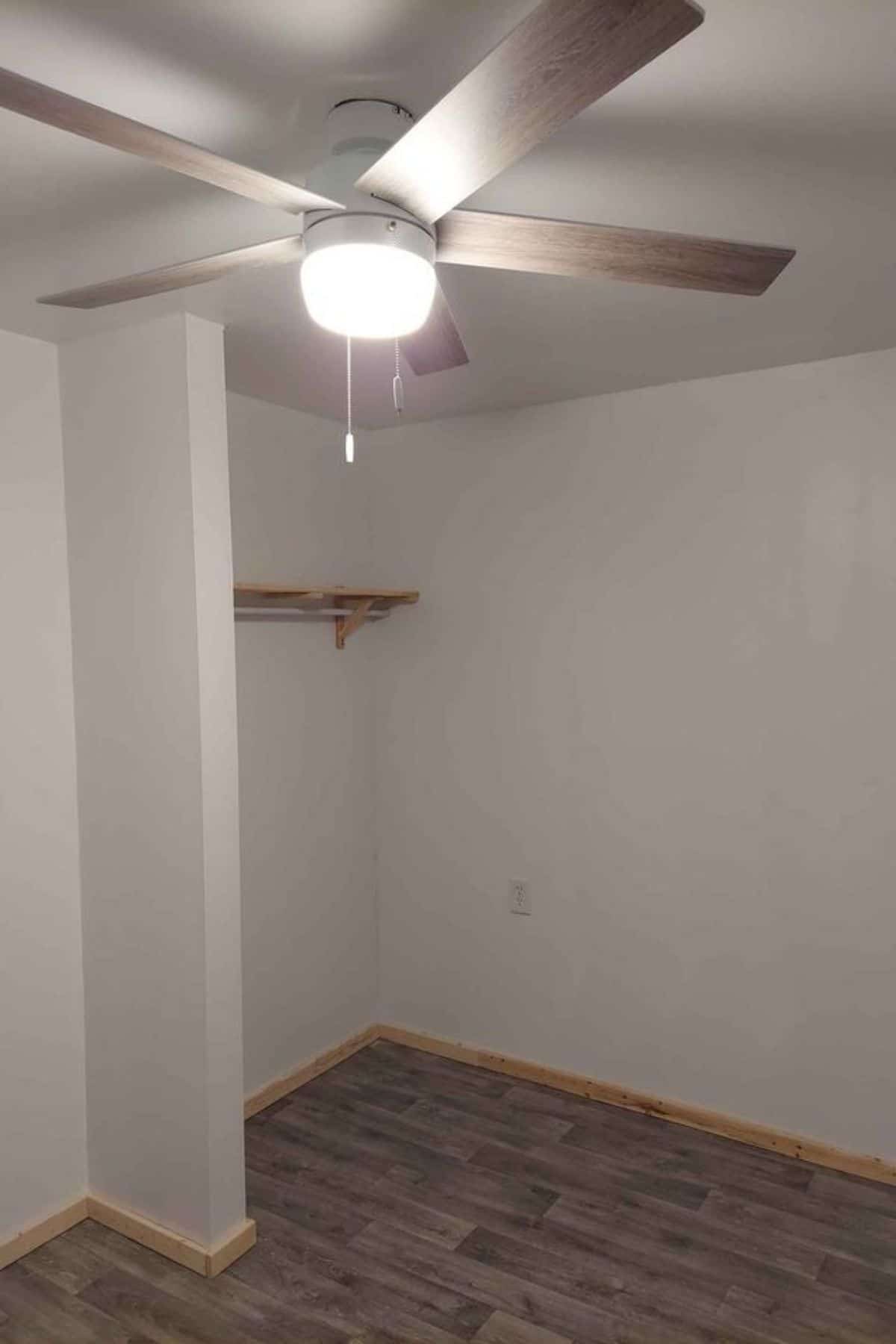 open closet against wall in tiny bedroom with white walls and gray flooring