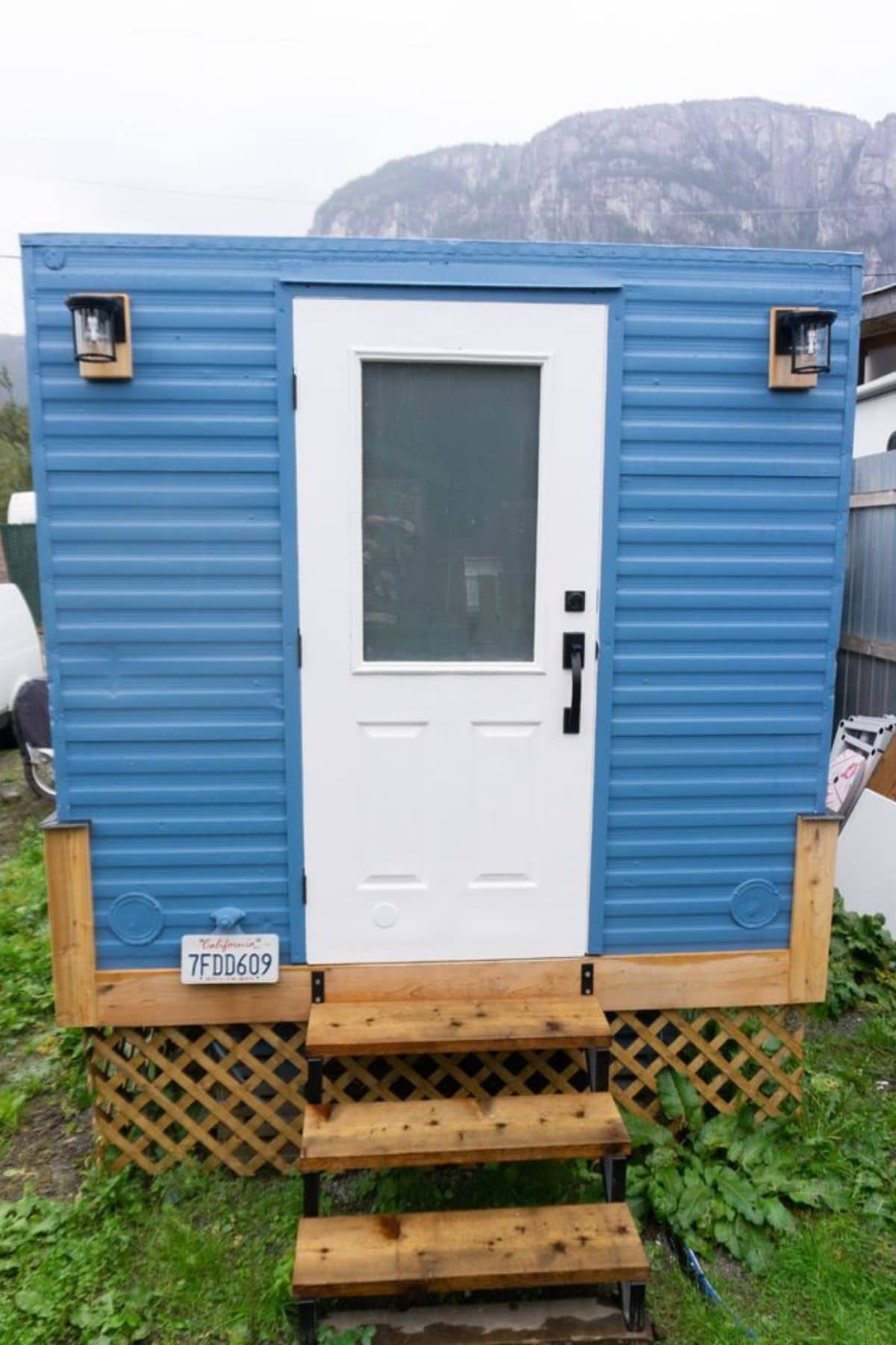 end of tiny home with blue siding and white door with wood steps