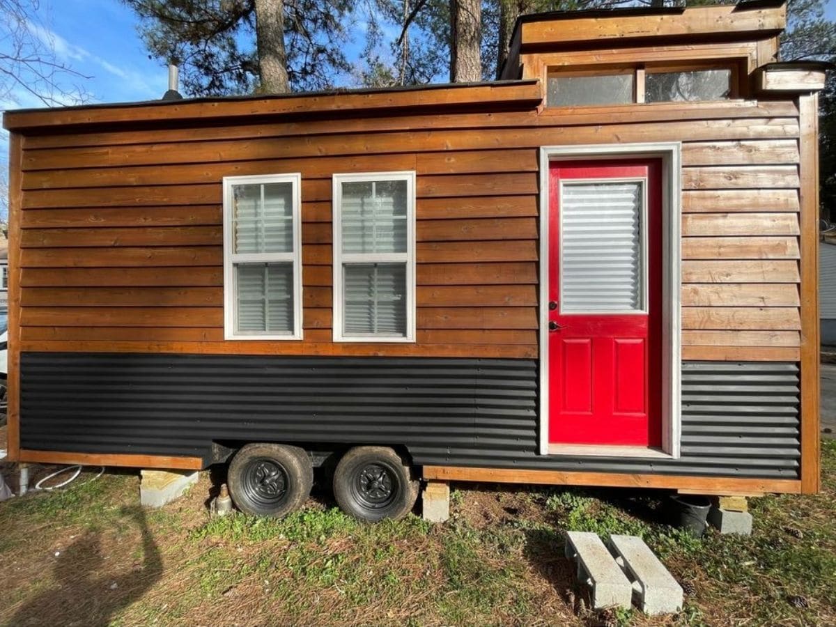 front of tiny home with two windows red front door and combination of wood and black siding