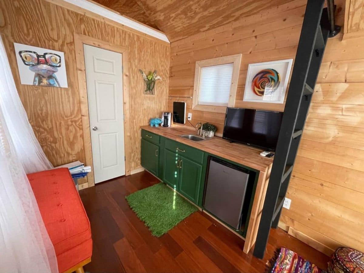 green rug in front of green kitchen cabinet in tiny home with black ladder at edge of counter