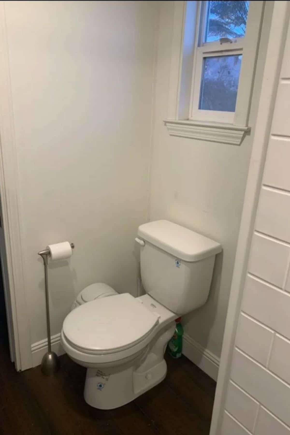 white flush toilet against white wall in bathroom below window
