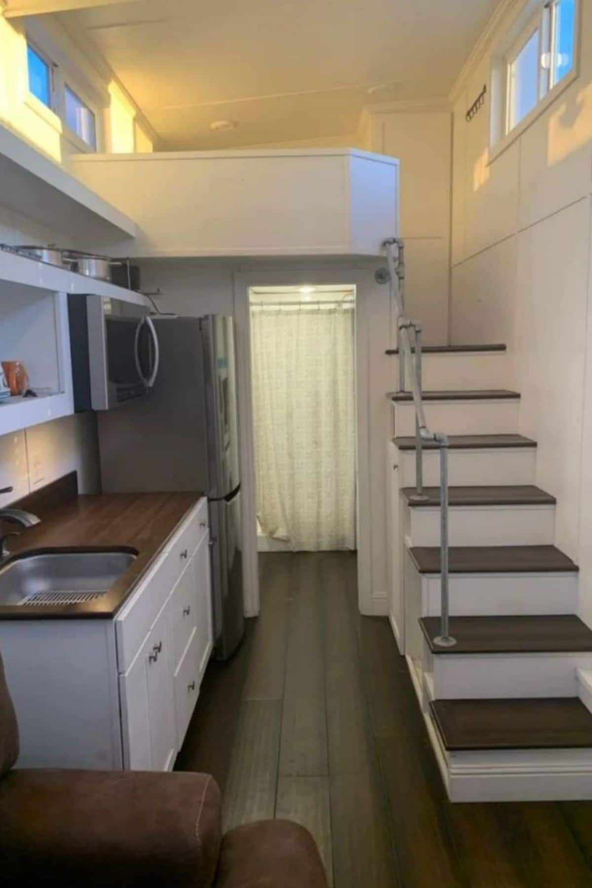 white stairs with gray tops on right of tiny home with white cabinets in kitchen to left