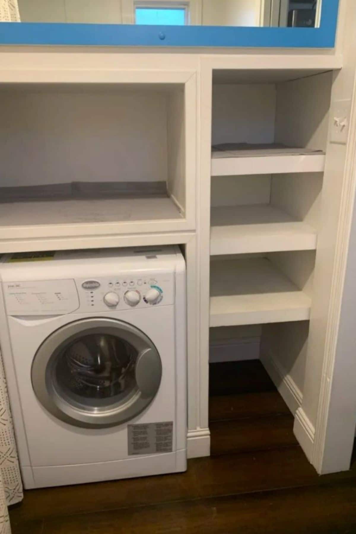 washing machine underneath white cabinets next to white open shelves