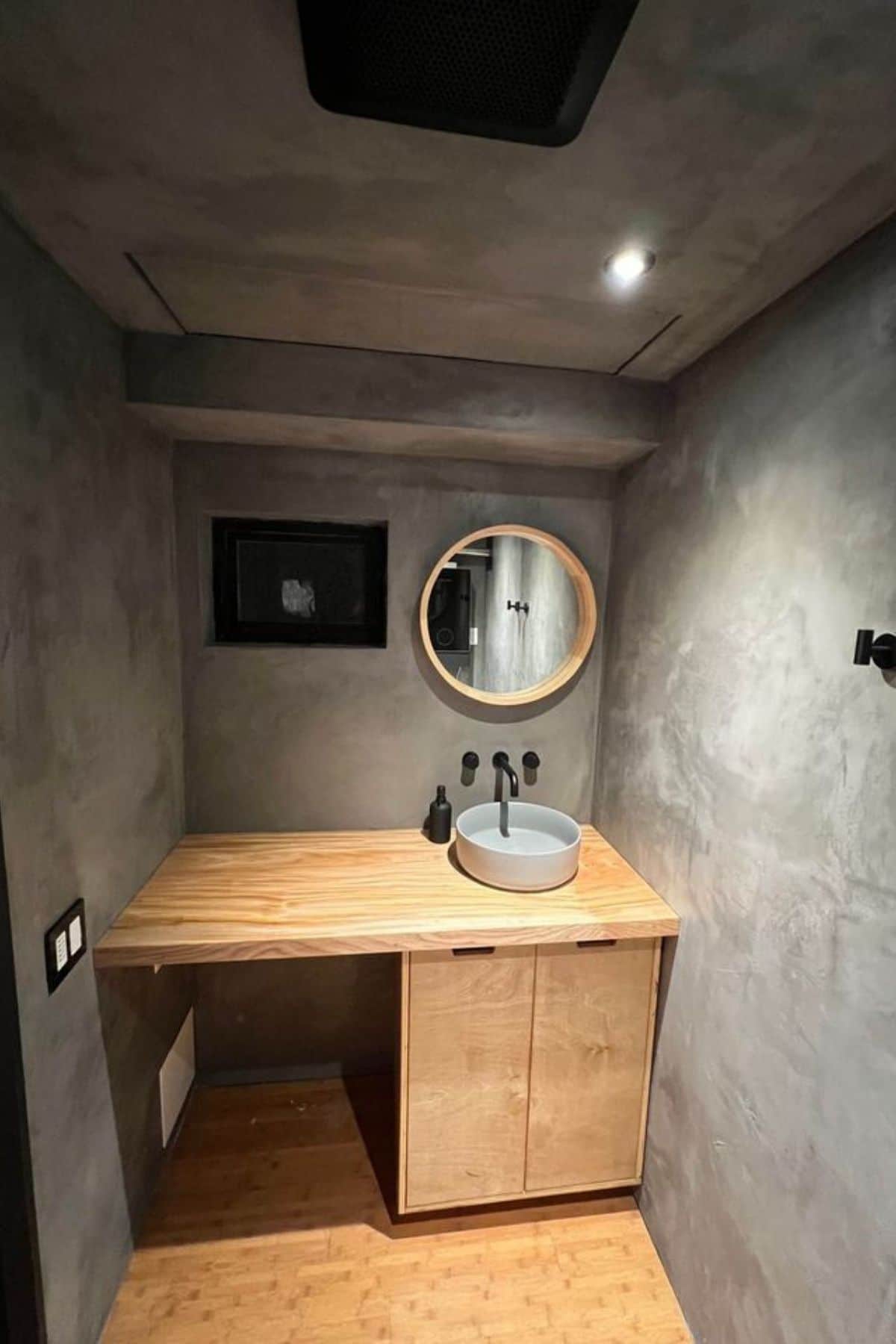 concrete wall with light wood vanity and white bowl sink in bathroom