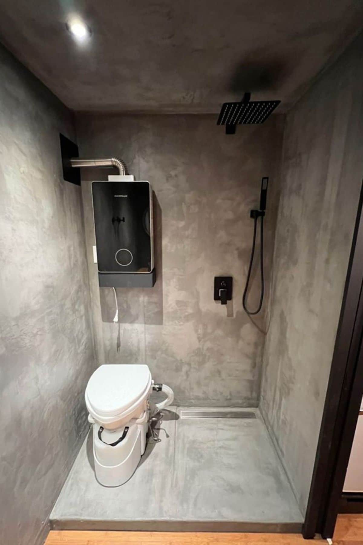 toilet inside concrete basin with shower head on far left corner